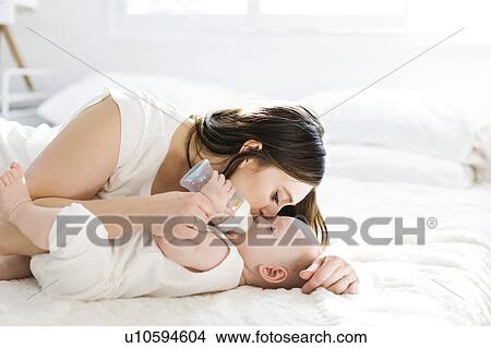 Picture - Mother kissing her son's cheek as he drinks bottle of milk. Fotosearch
