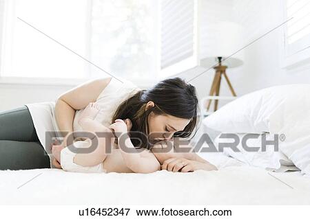 Mother kissing her son's cheek on bed View Large Photo Image Stock Photo - Mother kissing her son's cheek on bed. Fotosearch