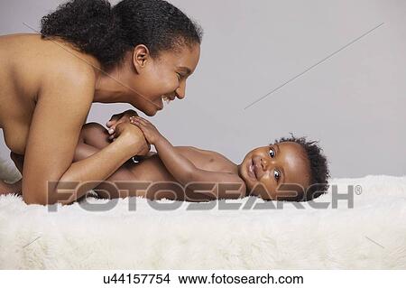Picture - Mother playing with baby lying on furry blanket. Fotosearch