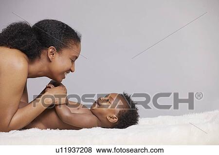 Stock Photo - Mother playing with baby lying on furry blanket. Fotosearch