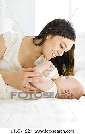 Stock Image - Mother watching her baby boy drink milk from bottle. Fotosearch