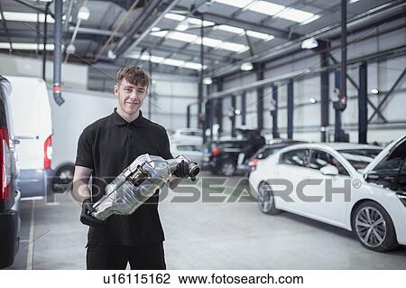 Stock Image - Portrait of apprentice engineer holding catalytic converter in car service centre. Fotosearch