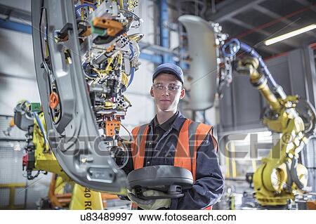 Stock Photo - Portrait of apprentice engineer programming robots in car factory. Fotosearch