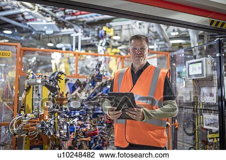 Stock Image - Portrait of computer programmer with robots in car factory. Fotosearch