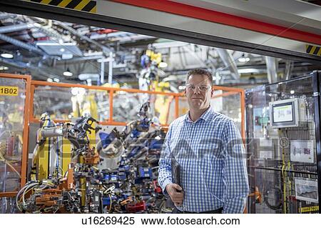 Stock Photography - Portrait of computer programmer with robots in car factory. Fotosearch