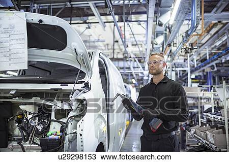 Stock Image - Portrait of engineer with drill on production line in car factory. Fotosearch