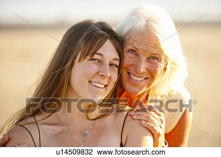 Stock Image - Portrait of mother and adult daughter smiling on beach. Fotosearch