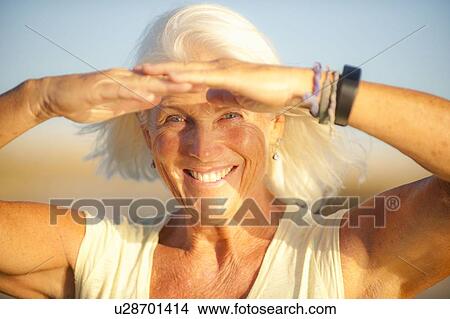 Picture - Portrait of smiling mature woman shielding her eyes. Fotosearch