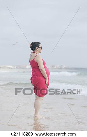 Stock Photo - Pregnant woman wearing pink dress on beach. Fotosearch