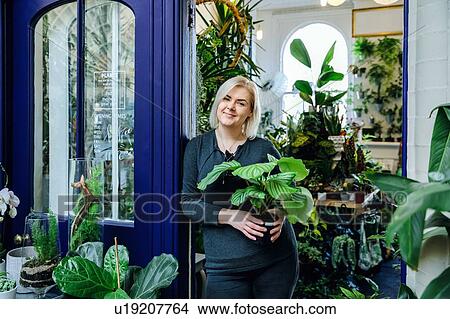Picture - Proud owner with potted plant, smiling in plant nursery. Fotosearch