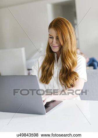 Stock Photo - Redheaded woman using laptop at home. Fotosearch