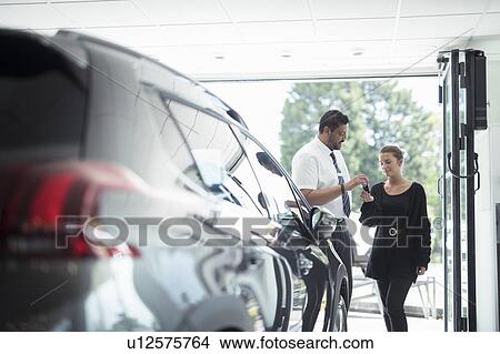 Salesman handing over new car keys to customer in car dealership View Large Photo Image Picture - Salesman handing over new car keys to customer in car dealership. Fotosearch