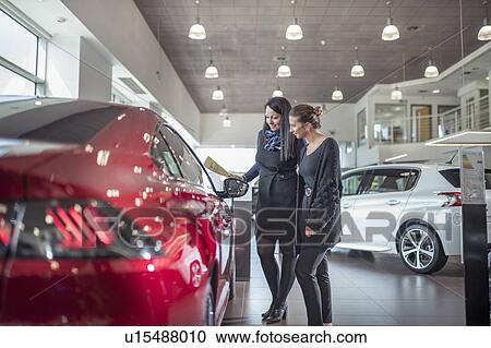 Stock Image - Saleswoman and customer inspecting new car in car showroom. Fotosearch
