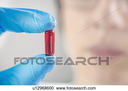 Stock Image - Scientist holding a red pill. Fotosearch