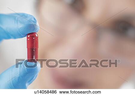 Stock Photograph - Scientist holding red pill. Fotosearch