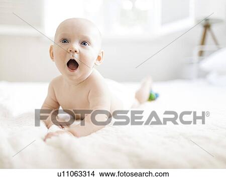 Picture - Shirtless baby boy lying on bed with his mouth open. Fotosearch