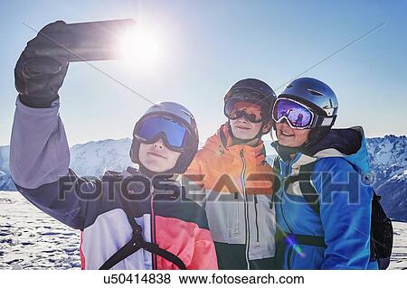 Stock Photo - Skiers, mother with teenage son and daughter taking selfie on snow covered mountain top, Alpe-d'Huez, Rhone-Alpes, France. Fotosearch