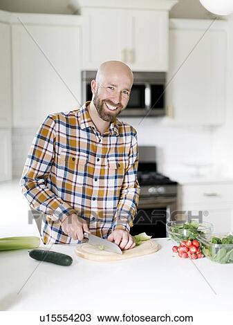 Stock Image - Smiling man chopping vegetables in kitchen. Fotosearch