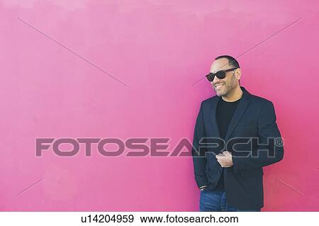 Stock Photo - Smiling man wearing sunglasses and blazer by pink wall. Fotosearch