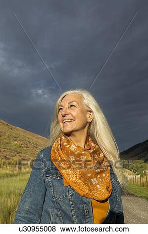 Stock Photo - Smiling mature woman wearing orange scarf in field. Fotosearch