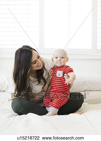 Smiling woman holding her son on bed View Large Photo Image Stock Image - Smiling woman holding her son on bed. Fotosearch