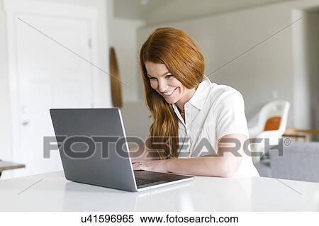 Stock Photography - Smiling woman using laptop at home. Fotosearch