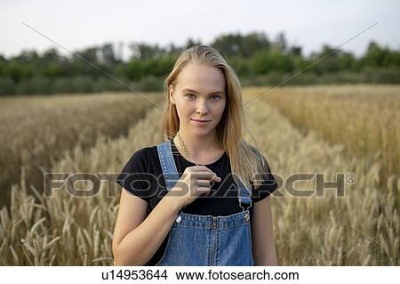 Picture - Smiling young woman holding wheat in field. Fotosearch