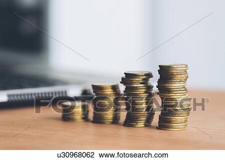 Stock Image - Stacked coins and laptop computer. Fotosearch