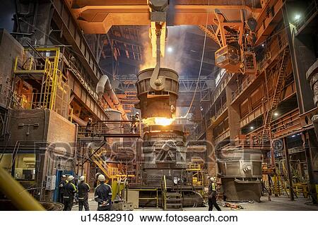 Stock Image - Steelworkers looking on during steel pour in steelworks. Fotosearch