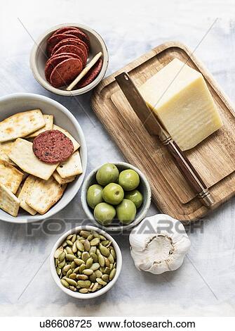 Still life of cutting board and cheese with bowls of crackers, olives, salami and pumpkin seeds, overhead view View Large Photo Image Stock Photography - Still life of cutting board and cheese with bowls of crackers, olives, salami and pumpkin seeds, overhead view. Fotosearch