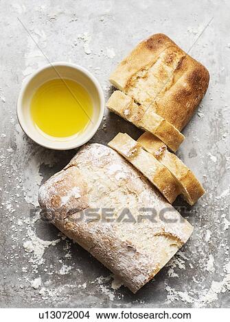 Picture - Still life of floured and unfloured ciabatta loaf on baking tray with bowl of olive oil, overhead view. Fotosearch