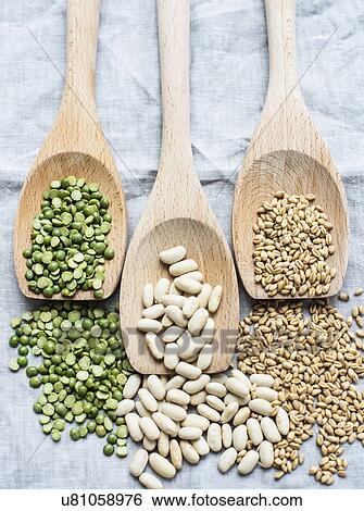 Stock Photograph - Still life of three wooden spoons green lentils, lima beans and pearl barley, overhead view. Fotosearch