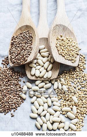 Stock Photo - Still life of three wooden spoons hemp seeds, lima beans and pearl barley, overhead view. Fotosearch