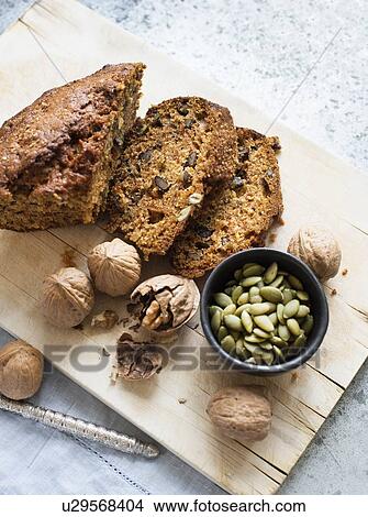 Picture - Still life of walnut and pumpkin seed cake sliced on cutting board, overhead view. Fotosearch