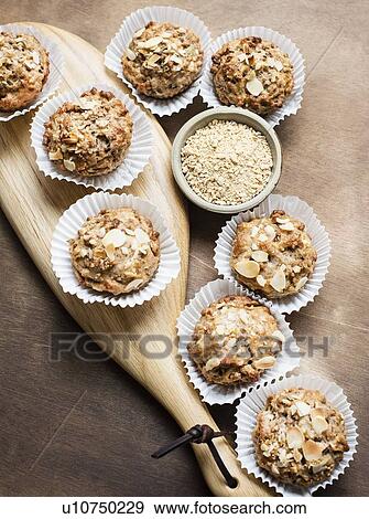 Stock Photo - Still life of wholemeal muffins on cutting board with bowl of oats, overhead view. Fotosearch