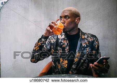 Stock Image - Stylish man enjoying drink, cellphone in hand. Fotosearch