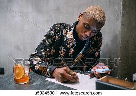 Stock Image - Stylish man enjoying drink while using laptop. Fotosearch