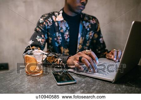 Stylish man enjoying drink while using laptop View Large Photo Image Stock Photography - Stylish man enjoying drink while using laptop. Fotosearch