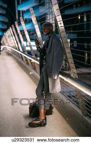 Stock Image - Stylish man leaning against bridge railings using cellphone, Milan, Italy. Fotosearch