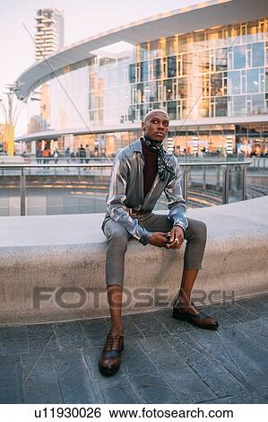 Stock Photograph - Stylish man sitting by water feature, Milan, Italy. Fotosearch