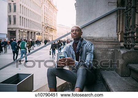 Stock Image - Stylish man sitting on steps of building, Milan, Italy. Fotosearch