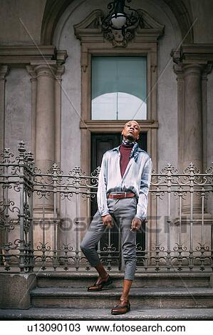 Stock Image - Stylish man standing on steps of period building, Milan, Italy. Fotosearch