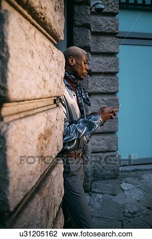 Stock Image - Stylish man using cellphone by period building, Milan, Italy. Fotosearch
