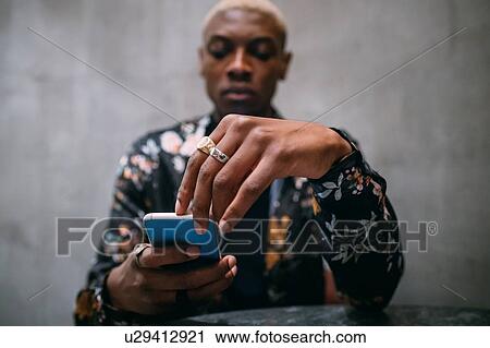 Stock Image - Stylish man using cellphone, concrete wall background. Fotosearch