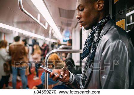 Stock Image - Stylish man using cellphone in train, Milan, Italy. Fotosearch