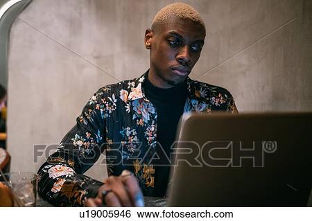 Stylish man using laptop, concrete wall background View Large Photo Image Stock Photograph - Stylish man using laptop, concrete wall background. Fotosearch