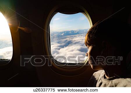 Stock Photography - Teenage boy looking out through airplane window at clouds on airplane journey. Fotosearch