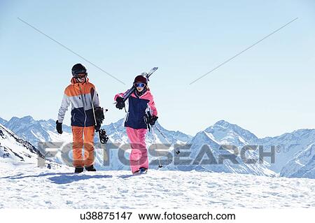 Stock Photo - Teenage boy snowboarder with sister skier walking on snow covered mountain top, Alpe-d'Huez, Rhone-Alpes, France. Fotosearch