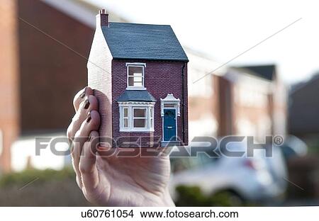 Picture - Teenage girl holding man made model of house in front of housing estate, shallow focus, close up of hand. Fotosearch