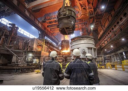 Stock Image - Three steelworkers watching molten steel pour in steelworks. Fotosearch